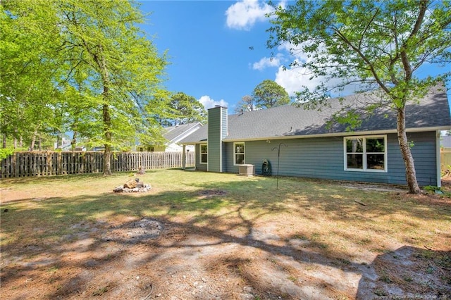 rear view of house with a lawn, a chimney, a fenced backyard, and central AC unit