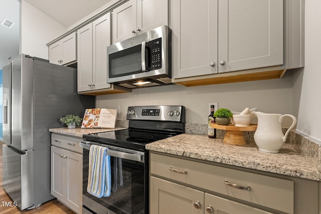 kitchen with light stone counters, stainless steel appliances, light wood-type flooring, and gray cabinets
