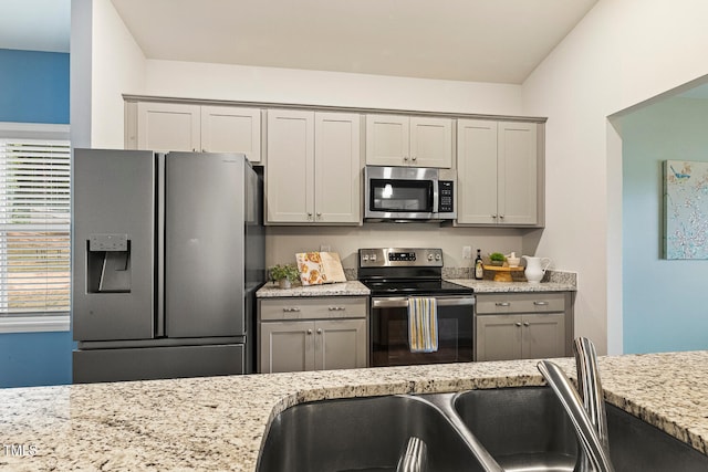 kitchen featuring stainless steel appliances, gray cabinetry, and light stone countertops