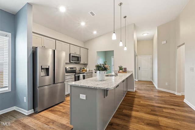 kitchen with a sink, gray cabinets, wood finished floors, a kitchen breakfast bar, and appliances with stainless steel finishes