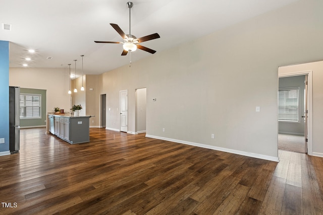 unfurnished living room with ceiling fan, a towering ceiling, baseboards, and dark wood finished floors