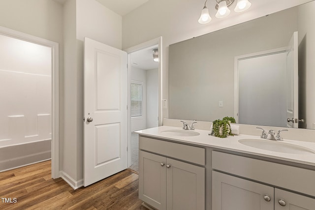 full bathroom featuring a bathing tub, double vanity, a sink, and wood finished floors