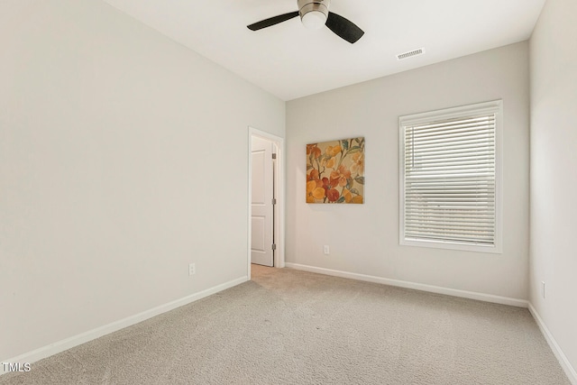 empty room with light colored carpet, visible vents, baseboards, and ceiling fan