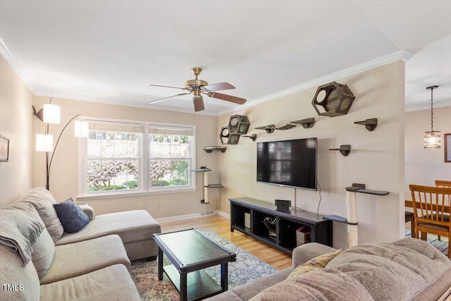 living room featuring ceiling fan, visible vents, wood finished floors, baseboards, and ornamental molding