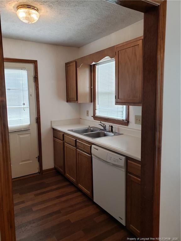 kitchen with a healthy amount of sunlight, a textured ceiling, dark wood finished floors, dishwasher, and a sink