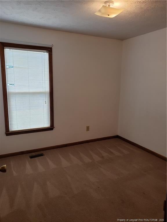 empty room with visible vents, a textured ceiling, carpet, and baseboards