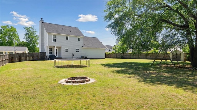 rear view of property with a trampoline, a shed, a fenced backyard, a chimney, and a fire pit