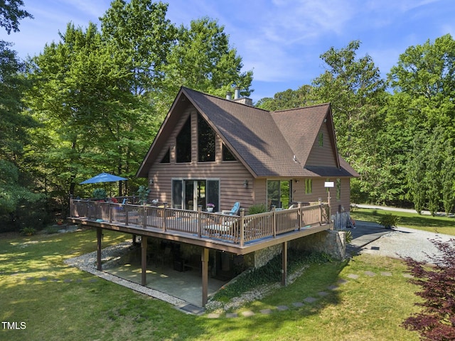 rear view of house with a deck, a lawn, roof with shingles, and a patio