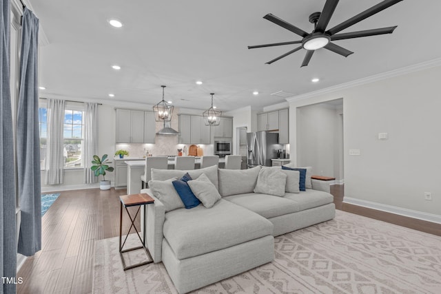 living room with ornamental molding, ceiling fan, recessed lighting, baseboards, and wood finished floors