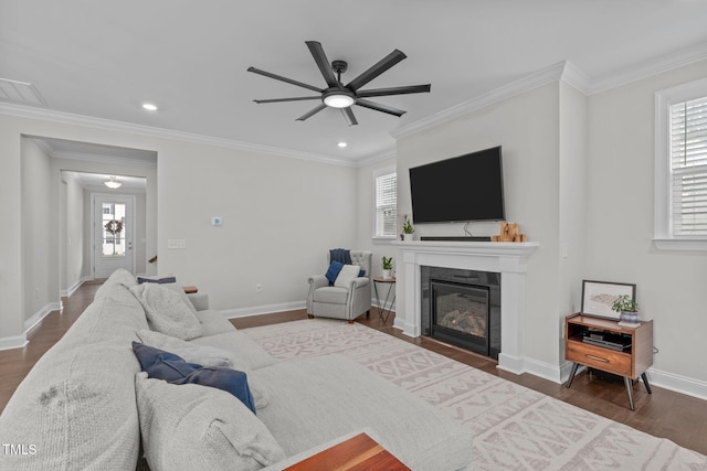 living room with healthy amount of natural light, ceiling fan, a tile fireplace, ornamental molding, and dark wood-style flooring
