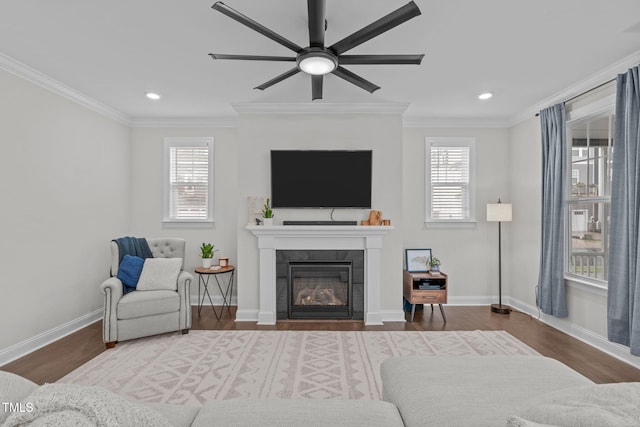 living area featuring ceiling fan, wood finished floors, crown molding, a tile fireplace, and baseboards