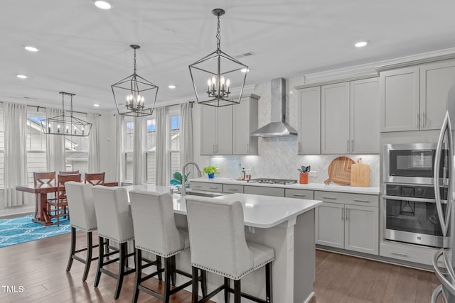 kitchen featuring wall chimney exhaust hood, appliances with stainless steel finishes, a chandelier, a sink, and plenty of natural light