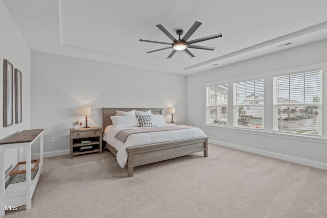 bedroom with light colored carpet, a raised ceiling, baseboards, and a ceiling fan