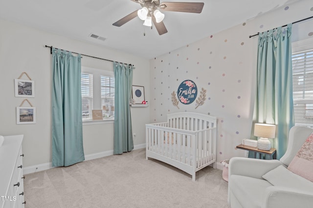 bedroom featuring light carpet, a nursery area, baseboards, and a ceiling fan
