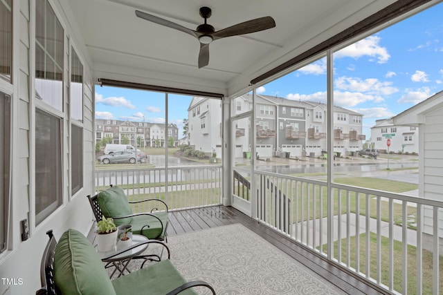 sunroom with a ceiling fan, a residential view, and a water view