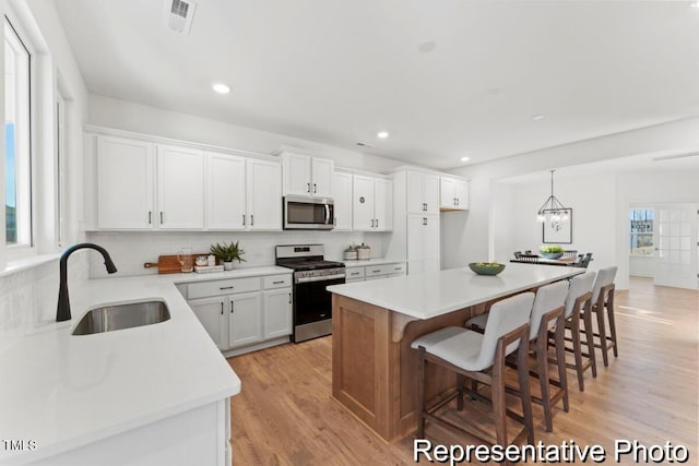 kitchen with a center island, a sink, white cabinets, visible vents, and appliances with stainless steel finishes