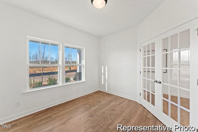 empty room with wood finished floors, french doors, and baseboards