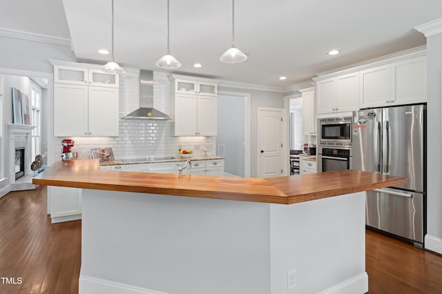 kitchen featuring stainless steel appliances, wall chimney range hood, butcher block counters, crown molding, and decorative backsplash