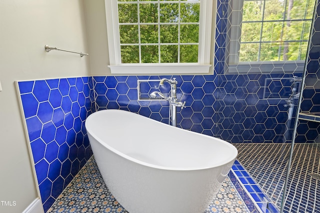 bathroom featuring tile walls, a freestanding bath, a tile shower, and wainscoting