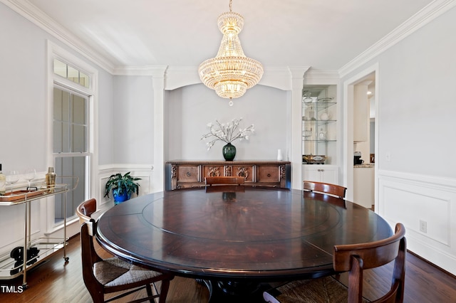 dining room featuring a chandelier, crown molding, wood finished floors, wainscoting, and a decorative wall