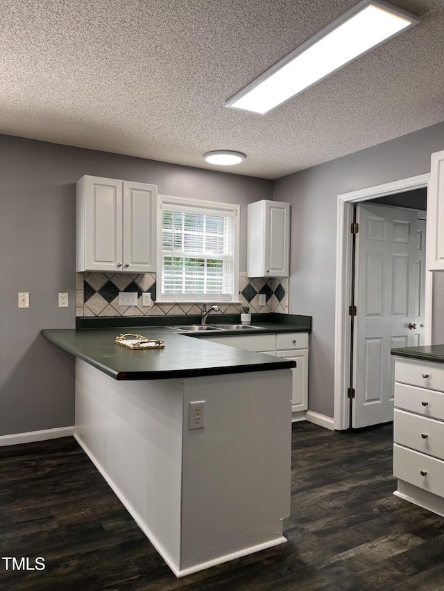 kitchen featuring a sink, a peninsula, tasteful backsplash, white cabinetry, and dark countertops