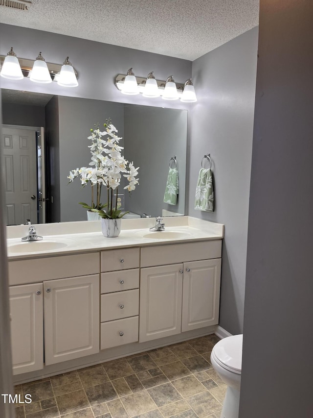 full bath with double vanity, toilet, a textured ceiling, and a sink