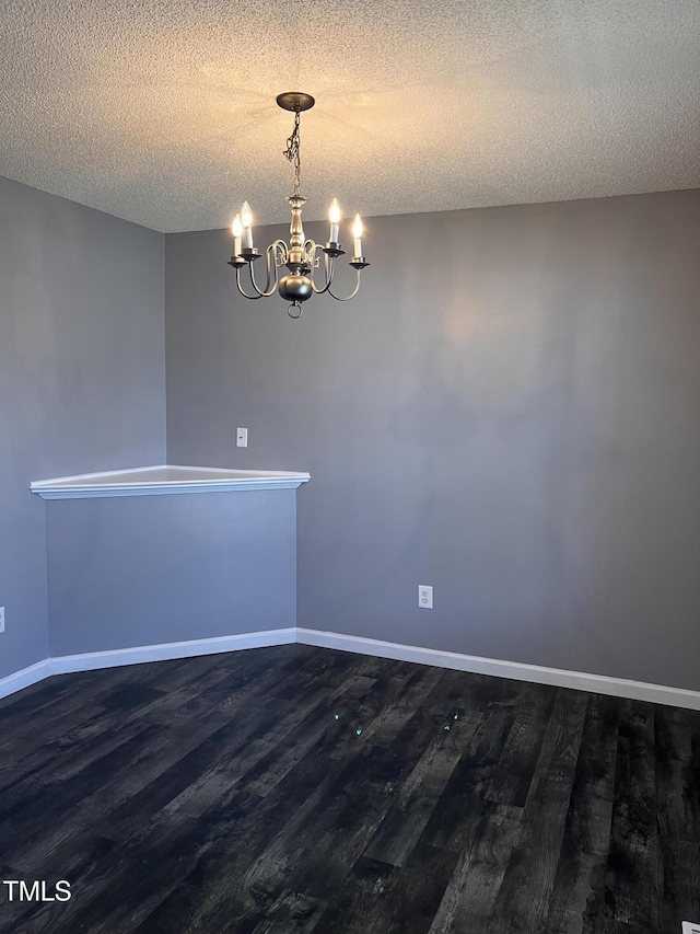 unfurnished room featuring an inviting chandelier, a textured ceiling, wood finished floors, and baseboards