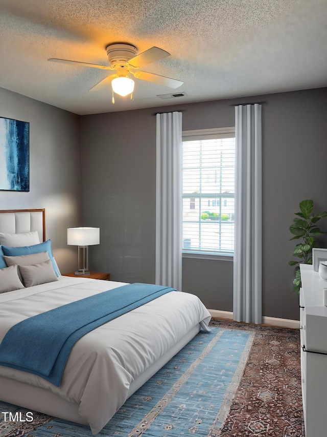 bedroom featuring ceiling fan, a textured ceiling, baseboards, and visible vents