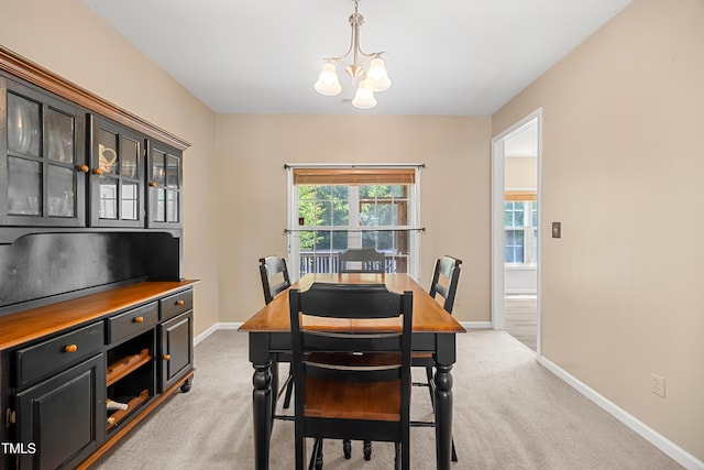 dining room with a chandelier, light colored carpet, and baseboards