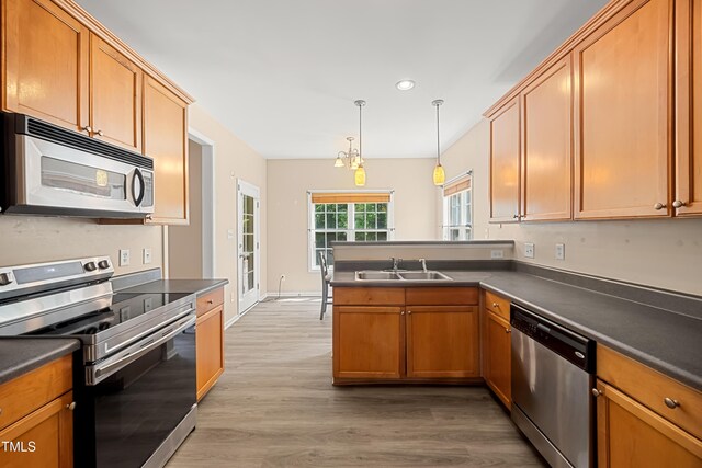 kitchen featuring stainless steel appliances, a sink, a peninsula, dark countertops, and light wood-type flooring
