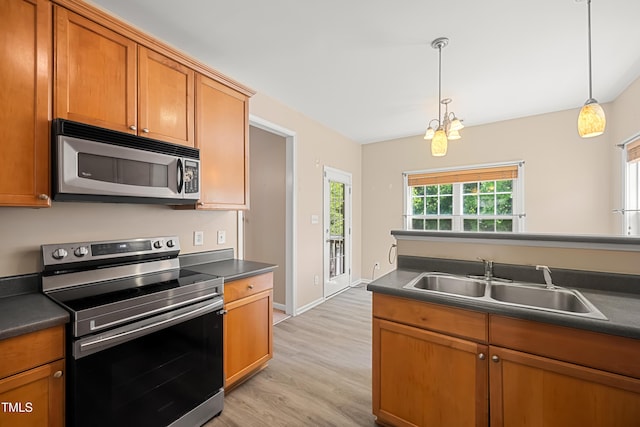 kitchen with appliances with stainless steel finishes, a sink, dark countertops, light wood-style flooring, and brown cabinets