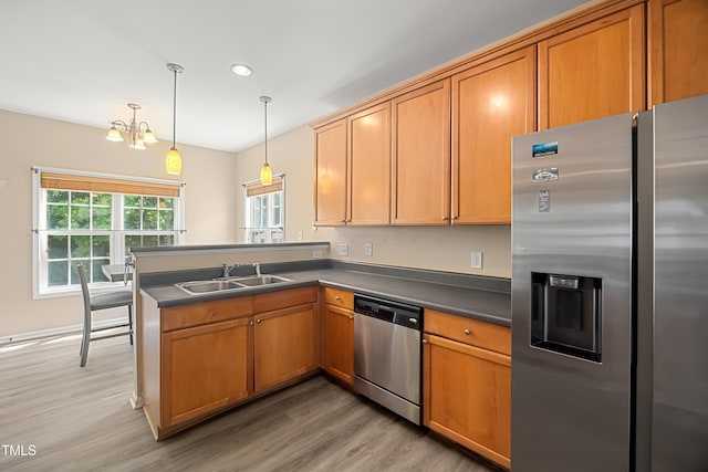 kitchen with stainless steel appliances, a sink, light wood finished floors, dark countertops, and a peninsula