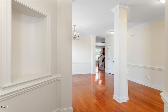 hallway with wood finished floors, ornate columns, baseboards, crown molding, and a chandelier
