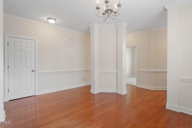 spare room with a chandelier, wood finished floors, baseboards, and ornamental molding