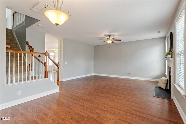 unfurnished living room featuring ceiling fan, wood finished floors, stairway, a fireplace with raised hearth, and plenty of natural light