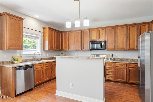 kitchen with appliances with stainless steel finishes, a sink, brown cabinets, wood finished floors, and recessed lighting