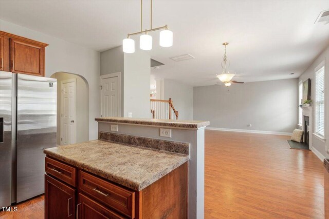 kitchen with stainless steel fridge with ice dispenser, a ceiling fan, light wood finished floors, arched walkways, and hanging light fixtures