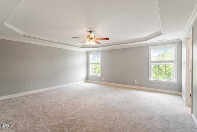 spare room with a tray ceiling, crown molding, light colored carpet, ceiling fan, and baseboards
