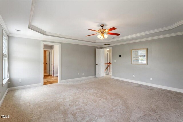 spare room featuring ornamental molding, a raised ceiling, light colored carpet, ceiling fan, and baseboards