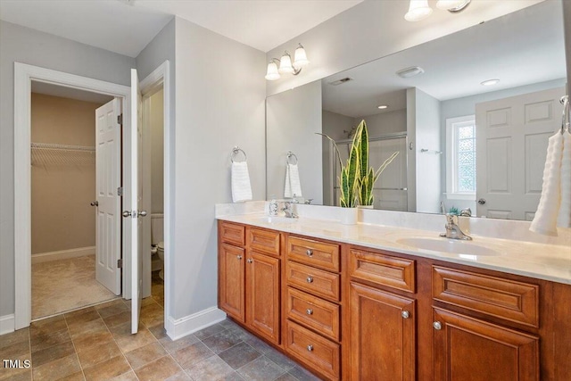 full bath with baseboards, double vanity, a shower with shower door, stone finish flooring, and a walk in closet