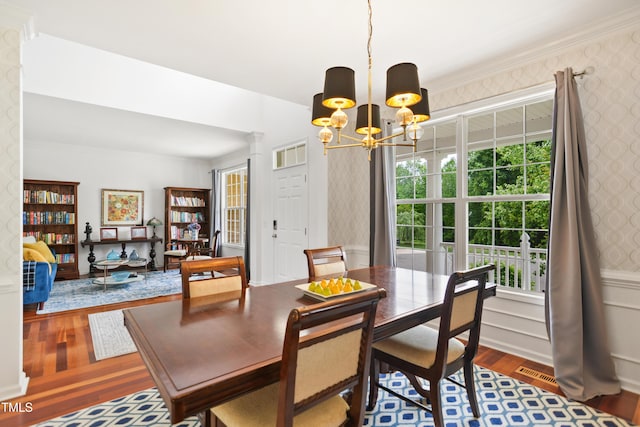 dining area with wood finished floors, wallpapered walls, a chandelier, healthy amount of natural light, and ornamental molding