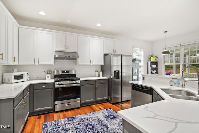 kitchen featuring appliances with stainless steel finishes, gray cabinetry, under cabinet range hood, a sink, and recessed lighting