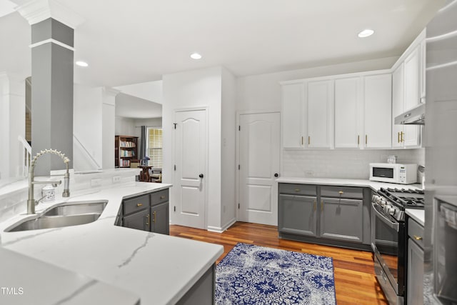 kitchen featuring stainless steel gas range, a sink, white microwave, gray cabinetry, and ornate columns