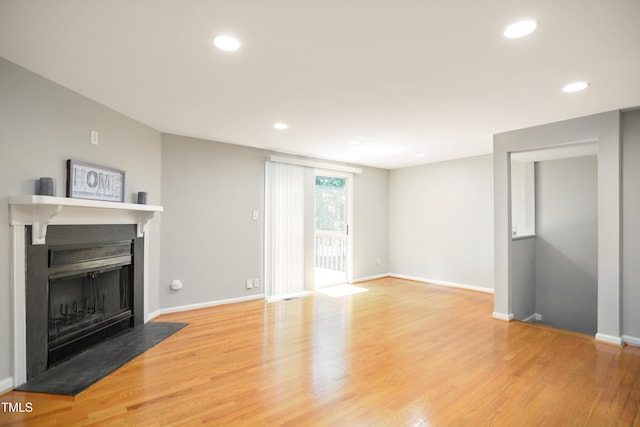 unfurnished living room with a fireplace with flush hearth, recessed lighting, light wood-style flooring, and baseboards