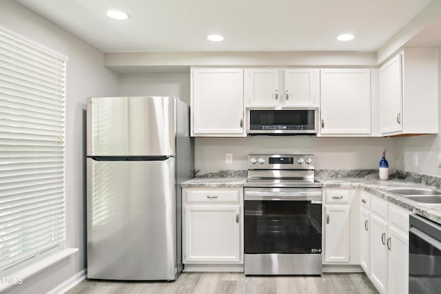 kitchen featuring stainless steel appliances, white cabinets, light wood-style floors, a sink, and recessed lighting