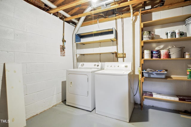 clothes washing area featuring washing machine and clothes dryer and concrete block wall