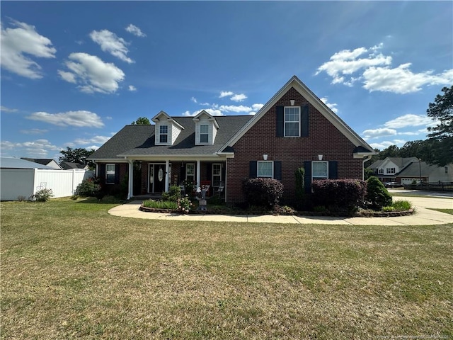 view of front of property with a front lawn, brick siding, covered porch, and fence