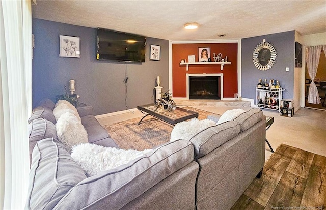 carpeted living room featuring a textured ceiling and a fireplace with raised hearth