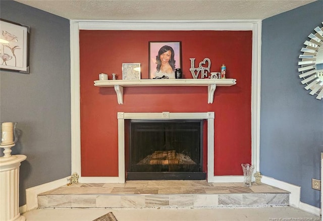details featuring baseboards, a textured ceiling, and a fireplace with raised hearth