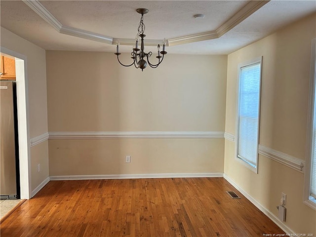 unfurnished dining area with a tray ceiling, wood finished floors, a healthy amount of sunlight, and a notable chandelier